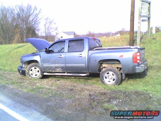 Blue pickup truck parked on grassy shoulder with hood up. Mud splatters on lower body