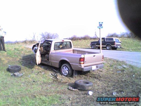Tan Ford Ranger pickup truck with open driver door and detached tire, parked off-road next to a black Ford Bronco SUV