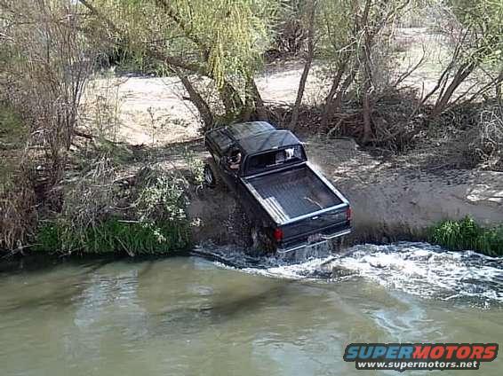 Black pickup truck with large tires driving through water