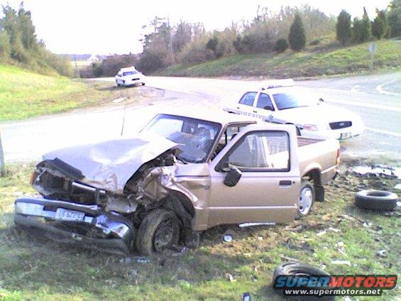 Front end of a gold pickup truck is smashed in, with police cars behind it on the side of the road