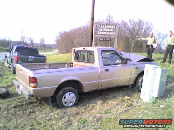 Tan pickup truck with damaged front end parked off-road near a church sign