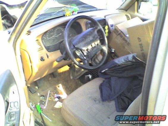 Interior of a damaged vehicle with a broken steering wheel and scattered tools on the floor