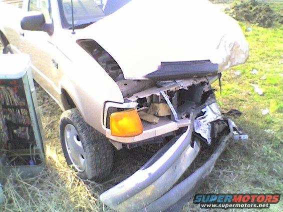 Front end damage on a beige pickup truck, hood open, bumper detached. Appears to be a 1990s model
