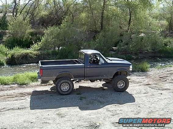 Dark blue 1992 Ford F-150 pickup truck with large tires parked by a river