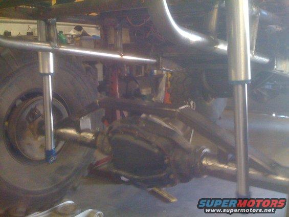 Off-road vehicle's rear axle, shocks, and suspension components. Large tire visible