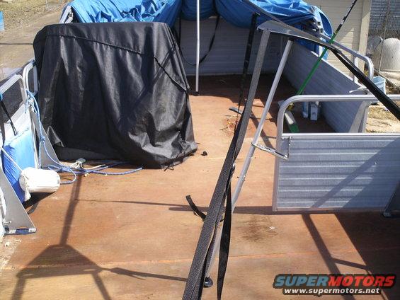 Pontoon boat deck with a black cover over an object, blue tarps, and metal railings