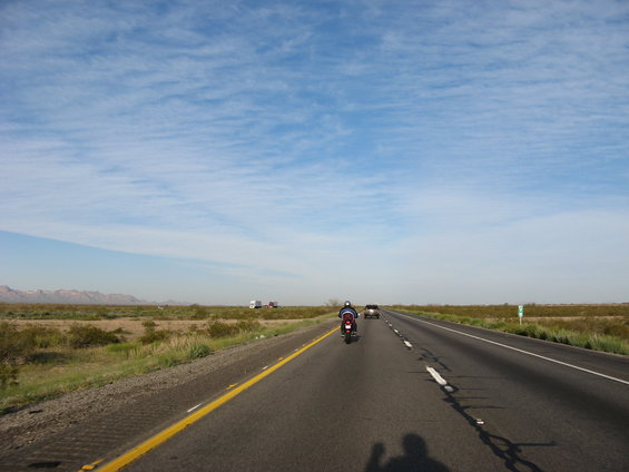 Motorcycle and car on a highway with desert landscape under a cloudy sky