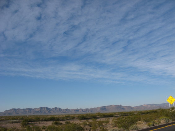 Desert landscape with mountains and a yellow 'Slowing Dust Area' sign