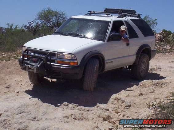 White SUV with a brush guard and roof rack driving on a dirt trail