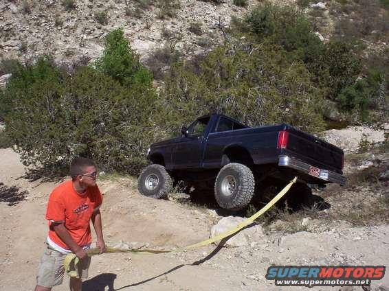 Black 1992 Ford F-150 pickup truck on a dirt incline with a yellow tow strap