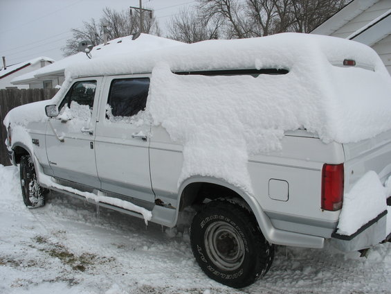 White extended cab pickup truck covered in snow, with a camper shell on the back