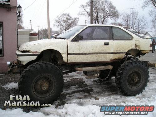 White car body on a custom chassis with massive off-road tires, parked in snow