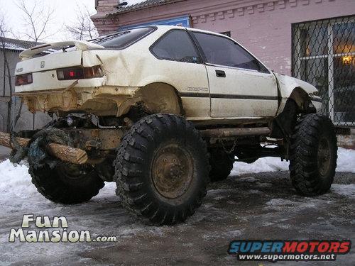 White Honda Civic coupe body on a lifted chassis with massive off-road tires, rear end is heavily modified
