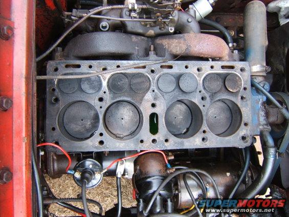 Engine block with visible valves and cylinders, red metal frame on left, wires and distributor visible