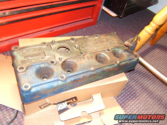 old engine valve cover with some blue paint and rust, sitting on cardboard