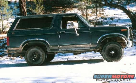 Dark green Ford Bronco parked in a snowy, wooded area. Side view shows its body style and large tires