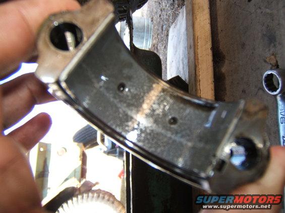 Hand holding a dirty engine bearing part with oil residue