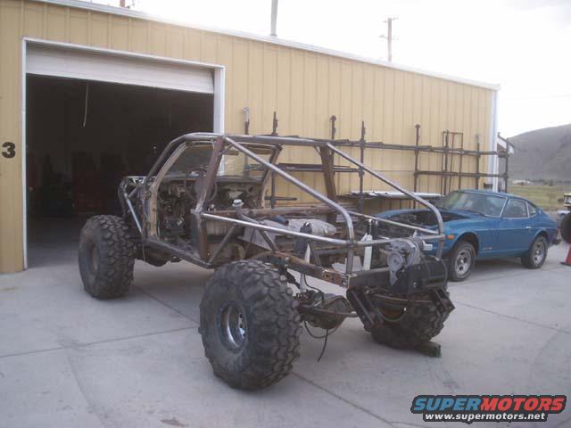 Off-road buggy project with custom roll cage and large tires, blue car in background
