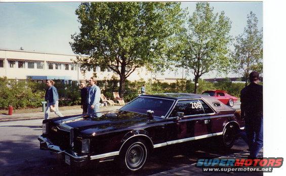 Dark red coupe with vinyl top, number 206 on the rear window, parked outside a building with trees