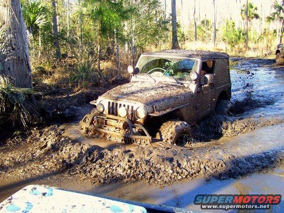Mud-covered 2004 Jeep TJ stuck in a muddy trail, front-left wheel deep in water