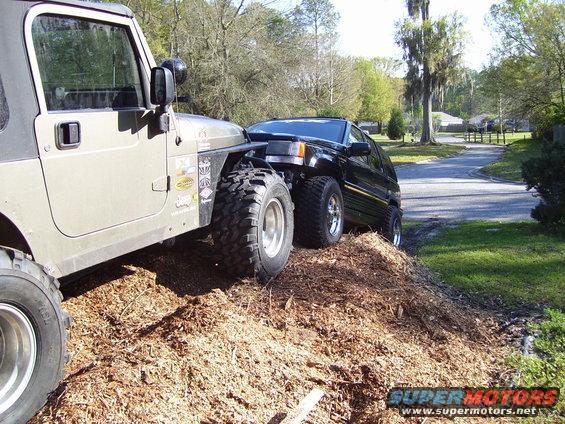 Tan Jeep Wrangler TJ with lifted suspension and aggressive tires, next to a black Jeep Grand Cherokee ZJ