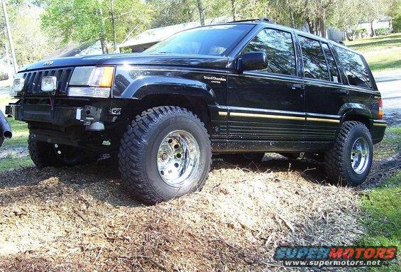 Black Jeep Grand Cherokee Limited with aftermarket wheels and tires, missing front bumper
