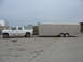 1995 Ford C-350 (Centurion Conversions) - A white Ford Bronco SUV is seen from the side, towing a long, silver, enclosed trailer on a paved lot.