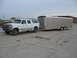 1995 Ford C-350 (Centurion Conversions) - A white Ford SUV conversion is parked next to a silver enclosed trailer on a concrete lot.