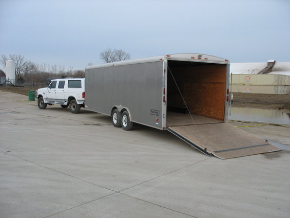 White 1990s Ford Bronco or similar SUV towing a grey enclosed cargo trailer with the rear ramp down