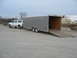 1995 Ford C-350 (Centurion Conversions) - A white SUV is parked next to a large, open cargo trailer on a paved lot.