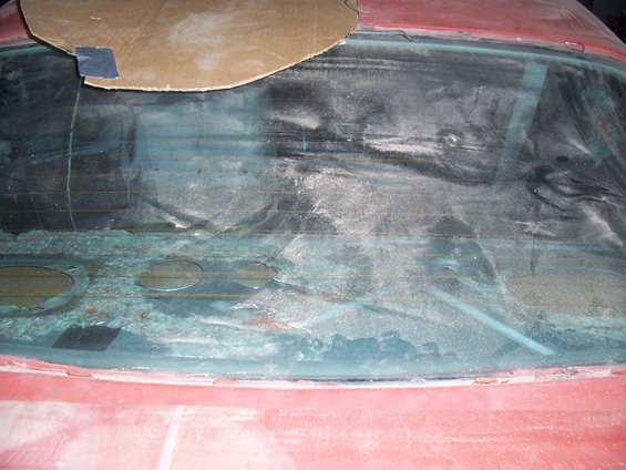 Rear window of a car covered in dust and debris, with cardboard taped to the top edge