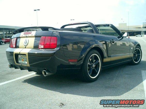 Black convertible Ford Mustang with gold stripes, rear view, showing spoiler and license plate