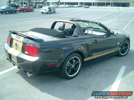 Black convertible Mustang with gold stripes, parked in a lot