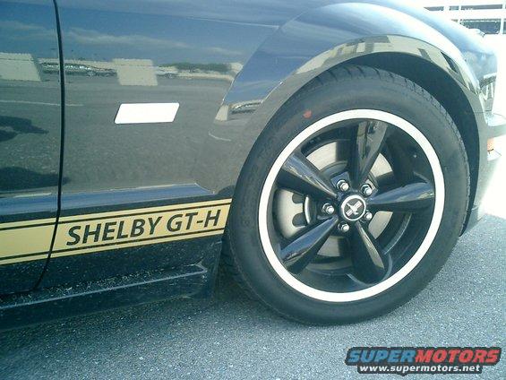 Side view of a black Shelby GT-H Mustang with gold stripes and a black five-spoke wheel