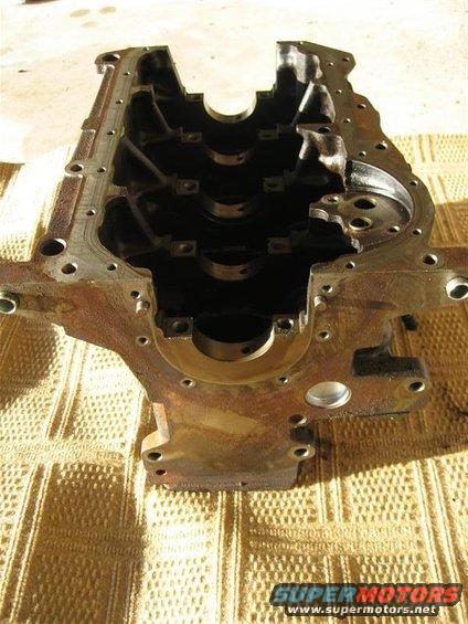 Engine block with bearing caps visible inside. The part is rusty and sits on a textured surface
