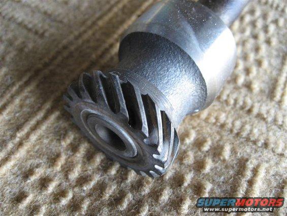 Close-up of a metal gear with helical teeth, resting on a textured surface
