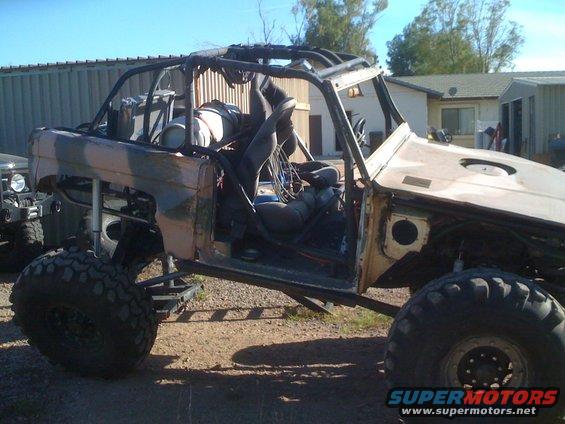 1966 Ford Bronco modified for off-roading, with roll cage and large tires. Another vehicle is partially visible to the left