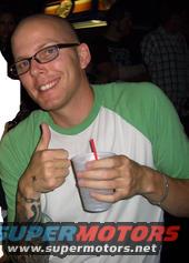 Man with glasses and a green and white shirt gives a thumbs up while holding a drink