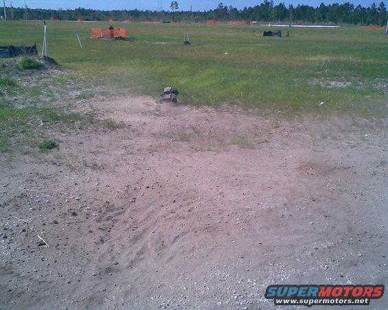 RC car kicking up dust on a dirt track, with construction fencing in the background