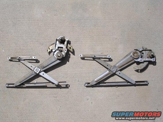 Two car window regulators with motors, laid out on concrete