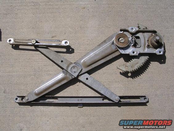 Car window regulator mechanism with gears and spring, lying on concrete