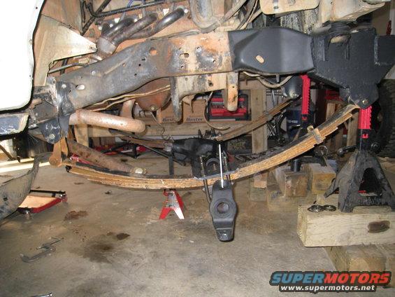 Undercarriage of a vehicle on jack stands, showing rusty leaf springs and suspension components