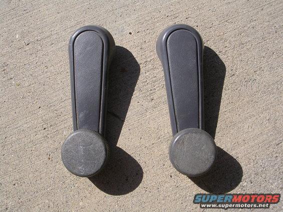 Two gray plastic window cranks with round knobs, lying on concrete