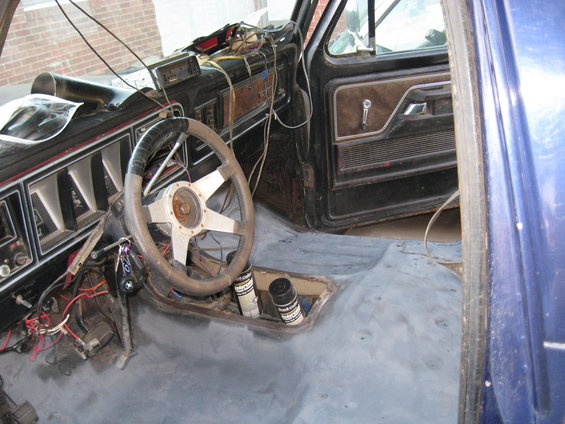 1978 Ford Bronco interior showing dashboard, steering wheel, and door panel. The floor is bare metal