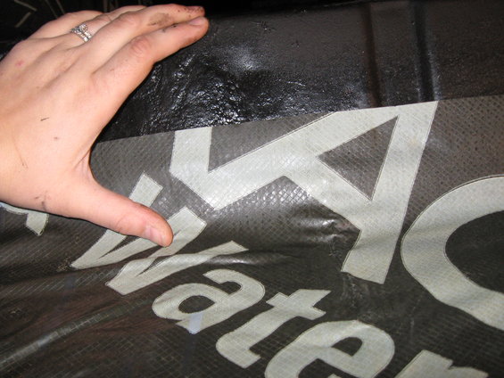 Waterproofing material with white text that reads 'Water'. Hand is holding the material