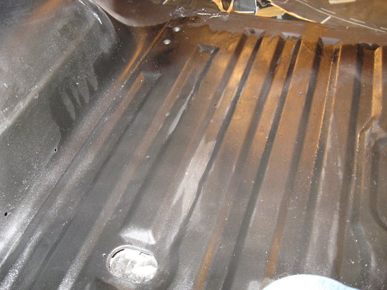 Black ribbed vehicle floor with some rust spots and a circular cutout