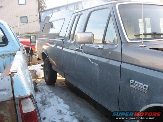 Side view of a gray 1990 Ford F-250 with a camper shell, parked next to another truck