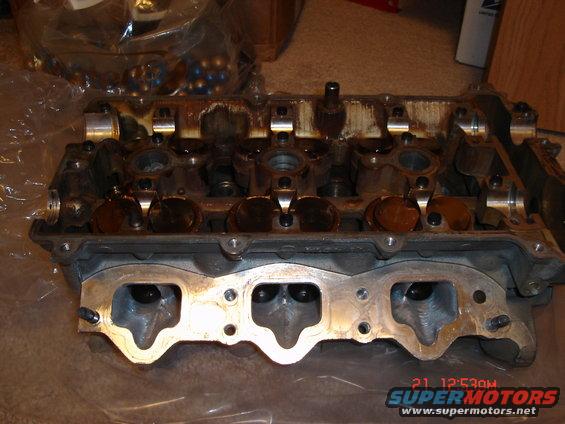 Engine cylinder head with valves and camshafts visible. Some oil residue is present