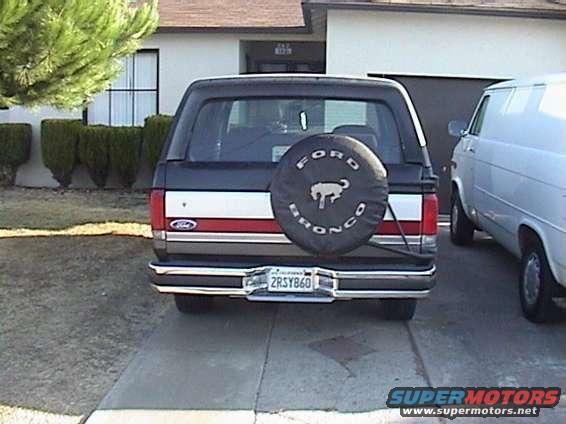 Rear view of a black Ford Bronco parked next to a white van. Spare tire on the back has 'Ford Bronco' text