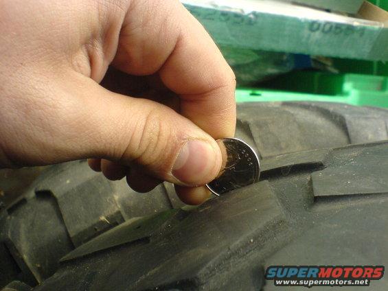 Hand holding a coin to measure tire tread depth on a large off-road tire